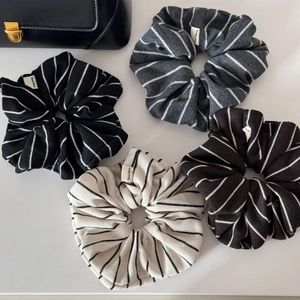 Detailed close-up of four striped fabric scrunchies in black, grey, brown, and cream