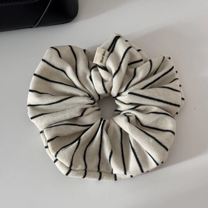 Close-up of a striped knit scrunchie with a handmade label on a minimal white surface