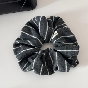 Detail of grey striped knit scrunchie with a Hand Made fabric label on minimal background