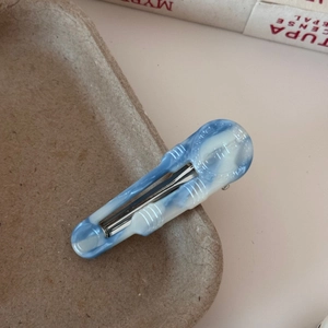 Detailed close-up of a blue and white marble pattern acetate duckbill hair clip on a tray