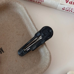 Detail of black acetate hair clip featuring a Girls circular motif with Greek key pattern