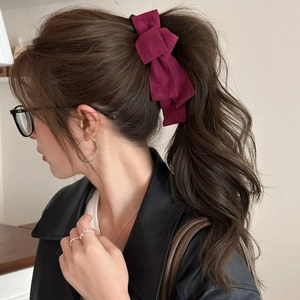 Detailed side view of a multilayered burgundy faux suede bow clip on a ponytail hairstyle