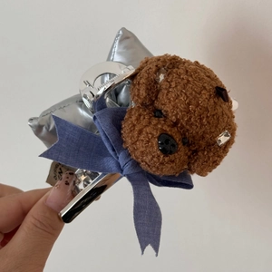 Dettaglio di un cucciolo in pile marrone e fiocco blu su una pinza per capelli in argento
