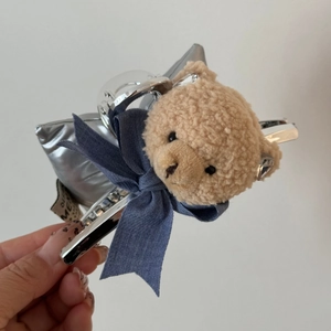 Dettaglio di orsetto di peluche e fiocco in denim su fermaglio per capelli in metallo