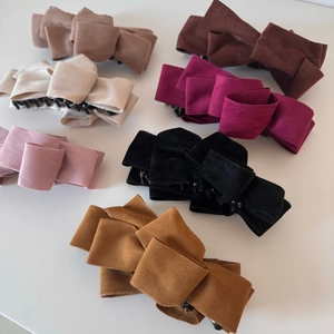 Detail showing seven colors of suede multi-layer bow banana hair clips on a white background