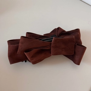Macro detail of multi-layer suede bow hair clip with textured fabric and inner teeth