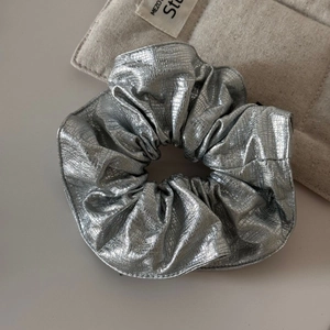Détail d'un chouchou en similicuir argenté avec motif serpent sur un sac matelassé