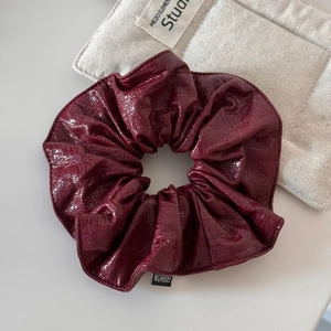 Détail d'un chouchou en similicuir bordeaux avec étiquette de mode et texture brillante