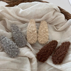 Detail of plush lamb wool BB hair clips in grey and brown on a soft fabric texture