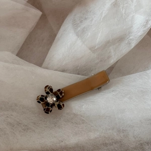 Detail of leopard print flower hair clip with sparkling rhinestone on white fabric
