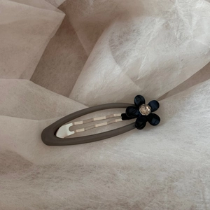 Close-up of matte grey oval hair clip featuring a black flower with a sparkling crystal