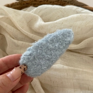 Close-up of light blue plush lambswool oval hair clip with soft curly texture detail