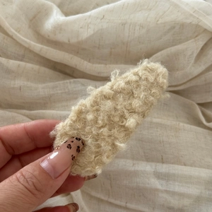 Close-up of a soft beige lamb wool hair clip featuring thick curly plush texture and detail