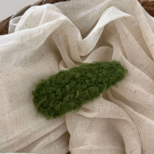 Close-up of forest green plush lamb wool BB hair clip on soft white textile background