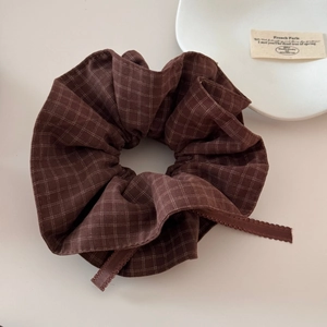 Detail of dark brown checkered scrunchie with scalloped lace edges on a minimalist background