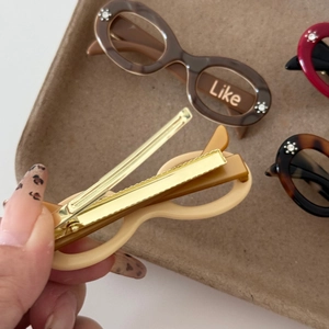 Detailed close-up of cream sunglasses-shaped acetate duckbill hair clip with rhinestones