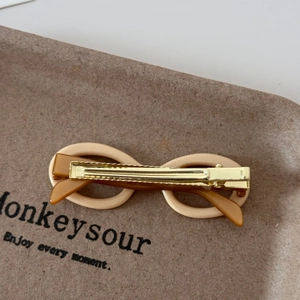 Detailed view of beige sunglasses-shaped acetate duckbill hair clip on a textured board