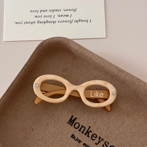 Detailed close-up of cream-colored acetate sunglasses-shaped hair clip with Like text