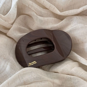 Détail d'une barrette en résine marbrée marron foncé avec lettrage doré sur tissu