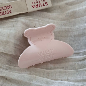 Makro-Detail einer rosa Haarklammer in Bärenform mit Gravur auf weichem Stoffhintergrund