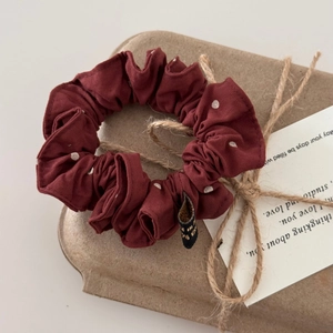 Dettaglio di uno scrunchie bordeaux a pois con etichetta su un vassoio rustico