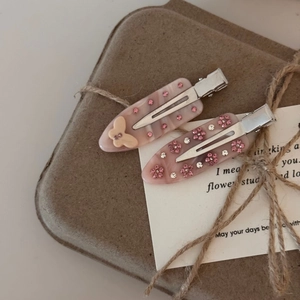 Détails de deux barrettes en acétate rose avec des papillons et fleurs en cristal