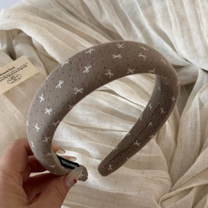 Close-up of taupe fabric headband with bow patterns and a black handmade textile label