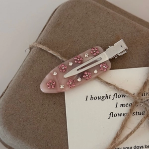 Détail d'une pince à cheveux en acétate avec fleurs en strass roses sur boîte cadeau
