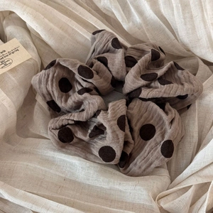 Detailed texture of brown fabric scrunchie with large black polka dots on beige background
