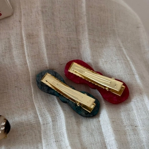 Close-up of two elegant acetate bow hair clips in red and marble blue on fabric