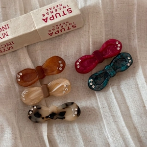 Detail of five assorted acetate bow hair clips with rhinestones on white fabric