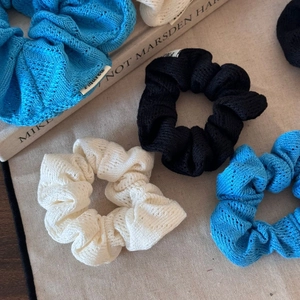 Trois chouchous en maille crochet bleu, noir et beige sur fond en toile
