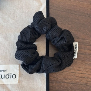 Détail d'un chouchou en tricot noir avec motif ajouré et étiquette de marque sur tissu