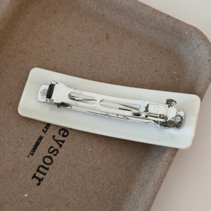 Detail of the silver metal spring clip structure on the white acetate hair clip
