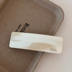Close-up of marble-textured cream acetate rectangular hair clip with gold engraving
