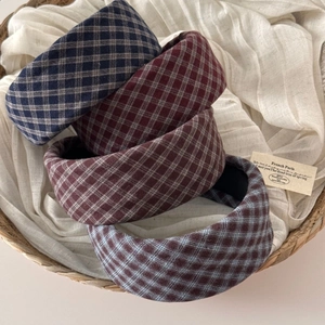 Close-up of four thick plaid headbands in assorted vintage colors on a linen cloth