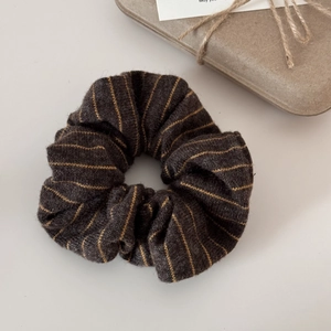 Close-up of a striped knitted scrunchie in charcoal grey and gold with gift packaging