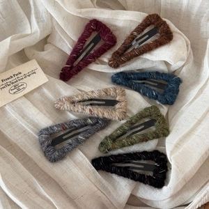 Detail of wool-wrapped triangular BB hair clips in autumn colors on beige fabric