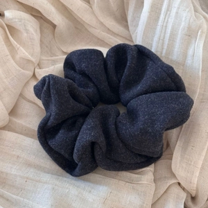 Detail view of large dark grey velvet scrunchie texture on a cream linen background