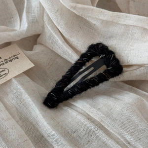 Close-up of black knitted wool hair clip with colorful speckled texture on linen
