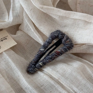 Detailed view of grey yarn-wrapped BB hair clip on a minimalist linen background