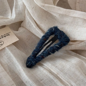 Detail of dark blue knitted yarn wrapped around a metal water drop hair clip texture