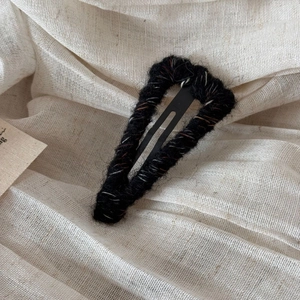 Detail of wool-wrapped triangle BB clip in black tweed yarn on a linen background