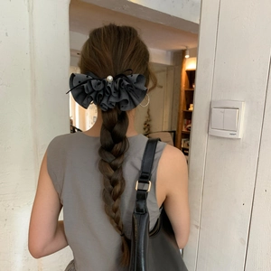 Macro shot of dark grey pleated bow hair clip with pearl detail on braided hair