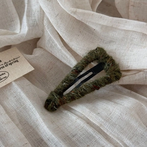 Macro shot of dark green wool wrapped triangular BB hair clip on a soft linen background