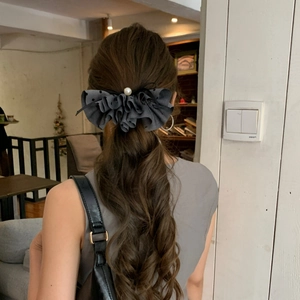 Detailed view of a grey pleated bow hair clip with a pearl center on wavy hair