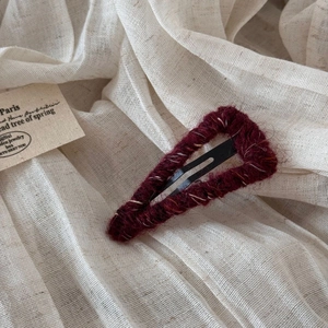 Detailed texture of burgundy wool wrapped triangular BB hair clip on a beige linen background