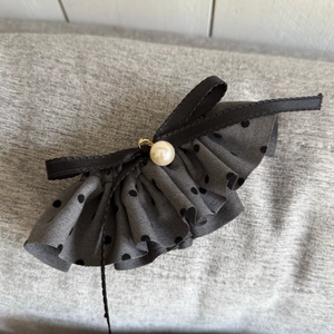 Detail of grey polka dot hair clip with ruffled fabric, black ribbon, and pearl accent