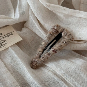 Close-up of a triangle BB hair clip wrapped in colorful woolen yarn on linen texture