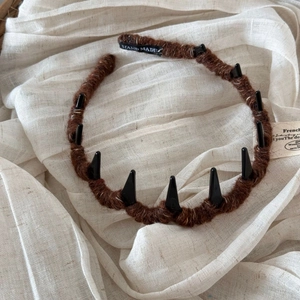 Brown knitted headband with black spikes and Hand Made label on fabric background